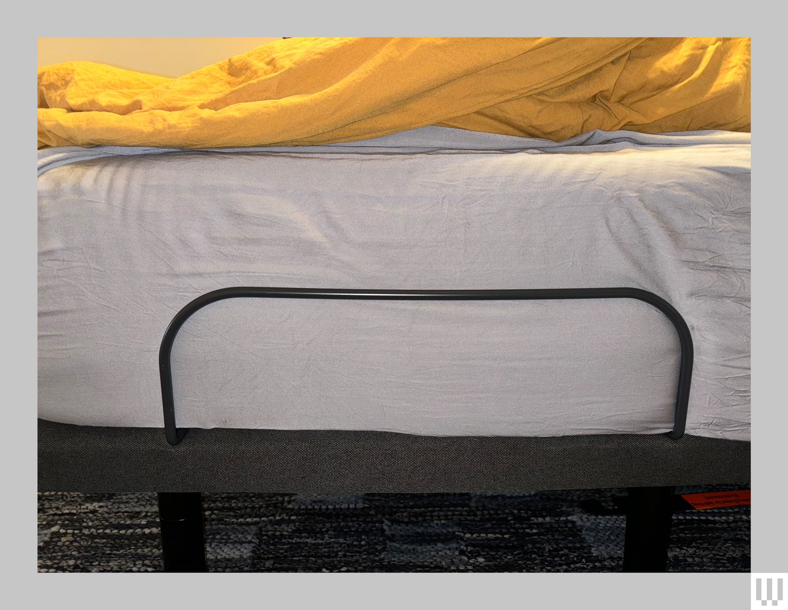 Side view of a thick mattress with a curved metal bar pressed to the side as part of the bed frame